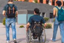 saude-adolescente-A imagem apresenta três adolescentes andando lado a lado. À esquerda um rapaz usando calça jeans, blusa verde e uma mochila, ao centro um rapaz na cadeira de rodas e com uma mochila e à direita uma adolescente usando jeans e blusa com listras brancas e amarelas e uma mochila verde. Ao fundo um prédio de uma escola.